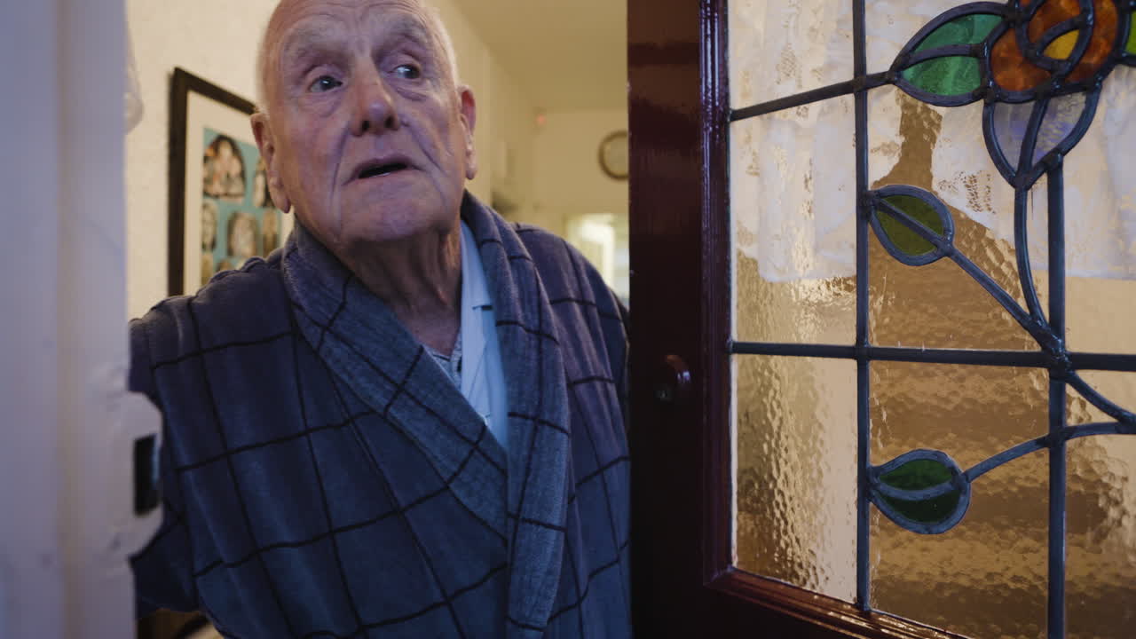 An elderly man in a robe standing in a doorway