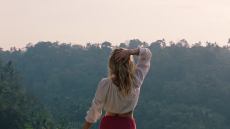 Mujer-Viajera-Celebrando-Con-Los-Brazos-Levantados-Mirando-La-Jungla-Tropical-Al-Amanecer-Sintiendo-Alegría-En-La-Aventura-De-Las-Vacaciones-De-Verano-Disfrutando-De-Un-Nuevo-Día-En-El-Paraíso