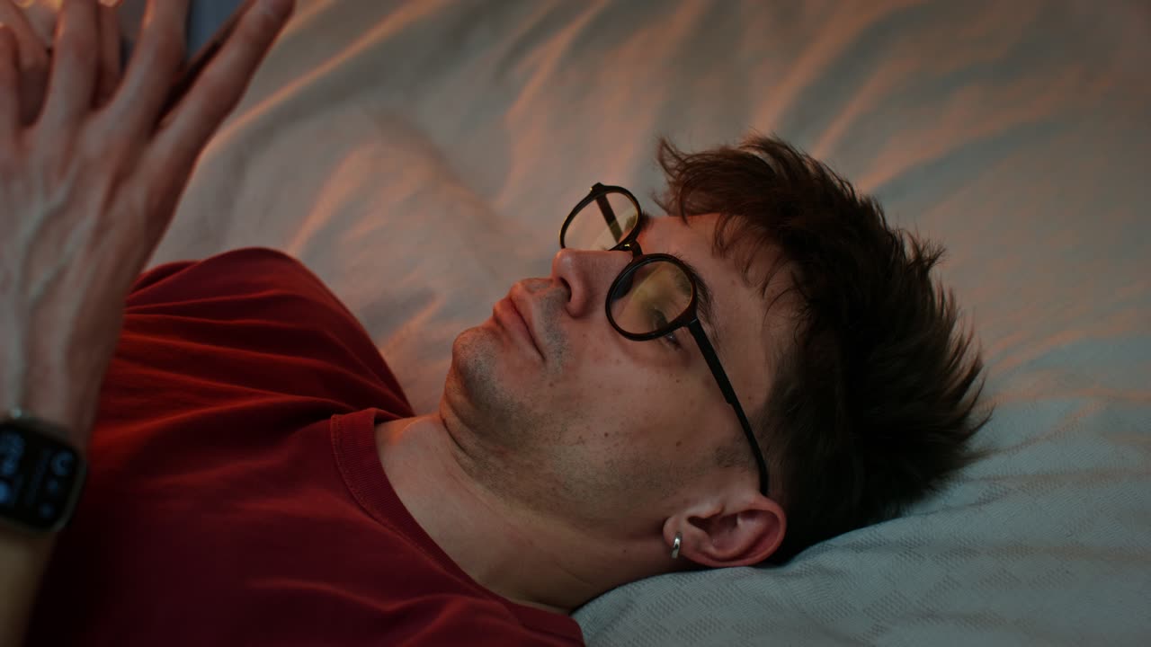 밤에 침대에서 스마트폰을 사용하는 남자