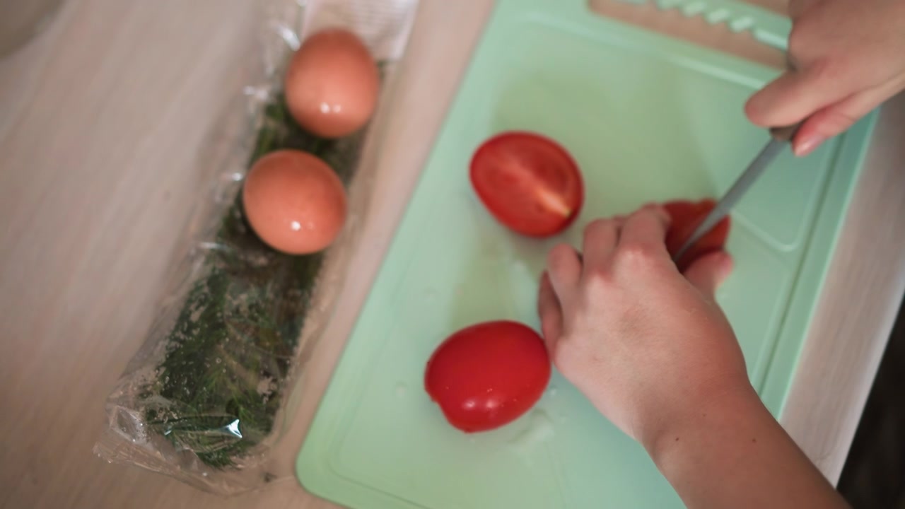 Scena di preparazione di verdure. Ingredienti per cucinare su un tagliere. Primo piano di mani che affettano un pomodoro fresco con un coltello. Preparazione di verdure con uova ed erbe aromatiche su una superficie da taglio da cucina.