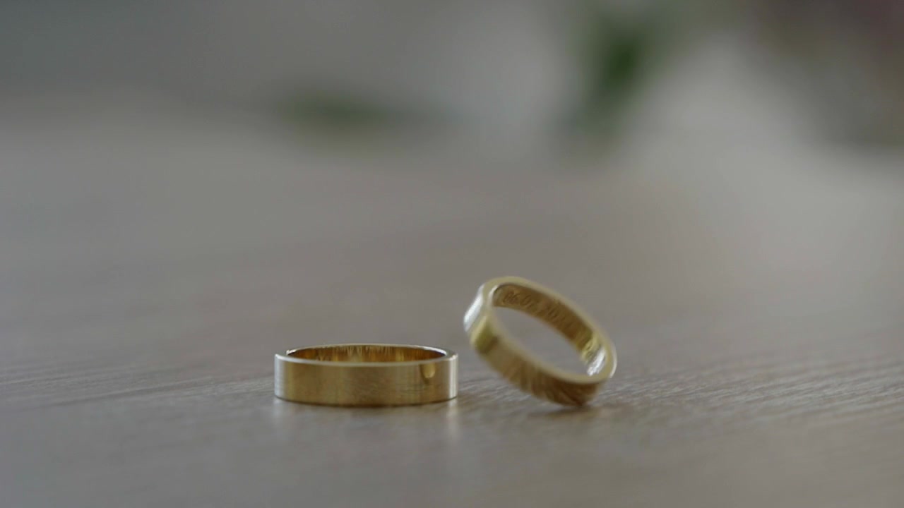 Close-up cincin pernikahan, dengan salah satunya berputar lalu berhenti di atas meja.