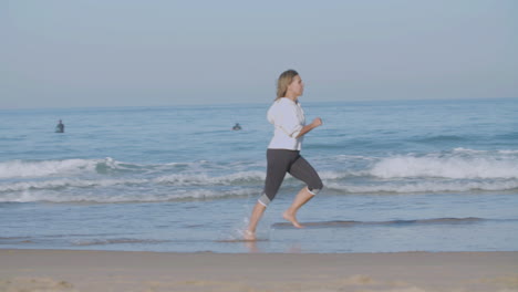 concentrated woman running barefoot fast along ocean coast