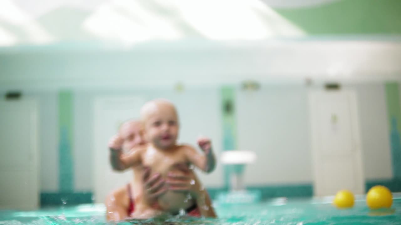 어머니가 수영을 가르치고 있는 동안 귀여운 금발 유아가 물  ⁇ 에 다이빙하고 있습니다.