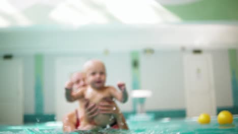 cute blonde toddler is diving under the water while his mother is holding him. his mother is teaching him how to swim. an underwater shot