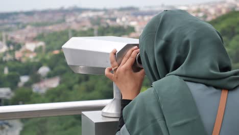 woman in hijab viewing cityscape through binoculars