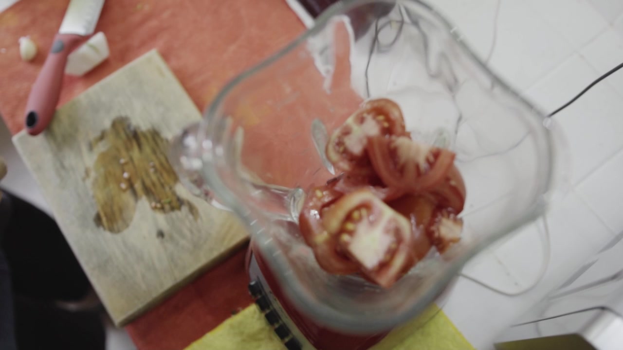 Vista superior de tomates frescos siendo colocados en el vaso de la licuadora durante el proceso de cocción, una escena de cocina sencilla que destaca la preparación de ingredientes para salsa o comida casera