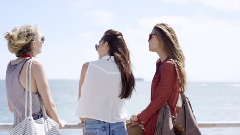 Teenage-girls-hanging-out-at-beach-on-summer-vacation-sitting-on-promenade-railing-shot-from-behind
