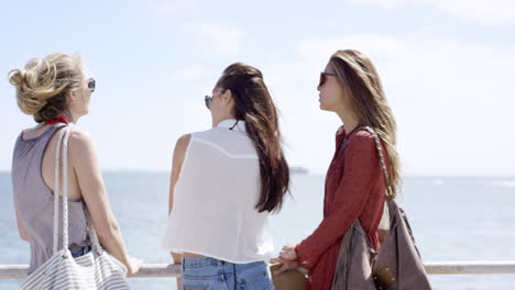 teenage girls hanging out at beach on summer vacation sitting on promenade railing shot from behind