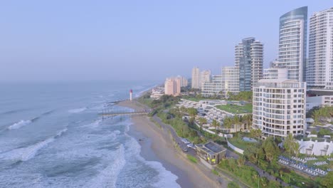 Costa-De-Umhlanga-Con-Edificios-Modernos-Y-Un-Faro,-Luz-De-Primera-Hora-De-La-Mañana,-Vista-Aérea