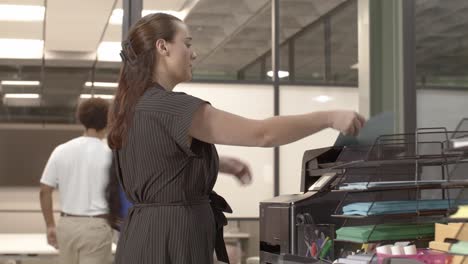 caucasian woman at a printer in a busy office with video moving right to left