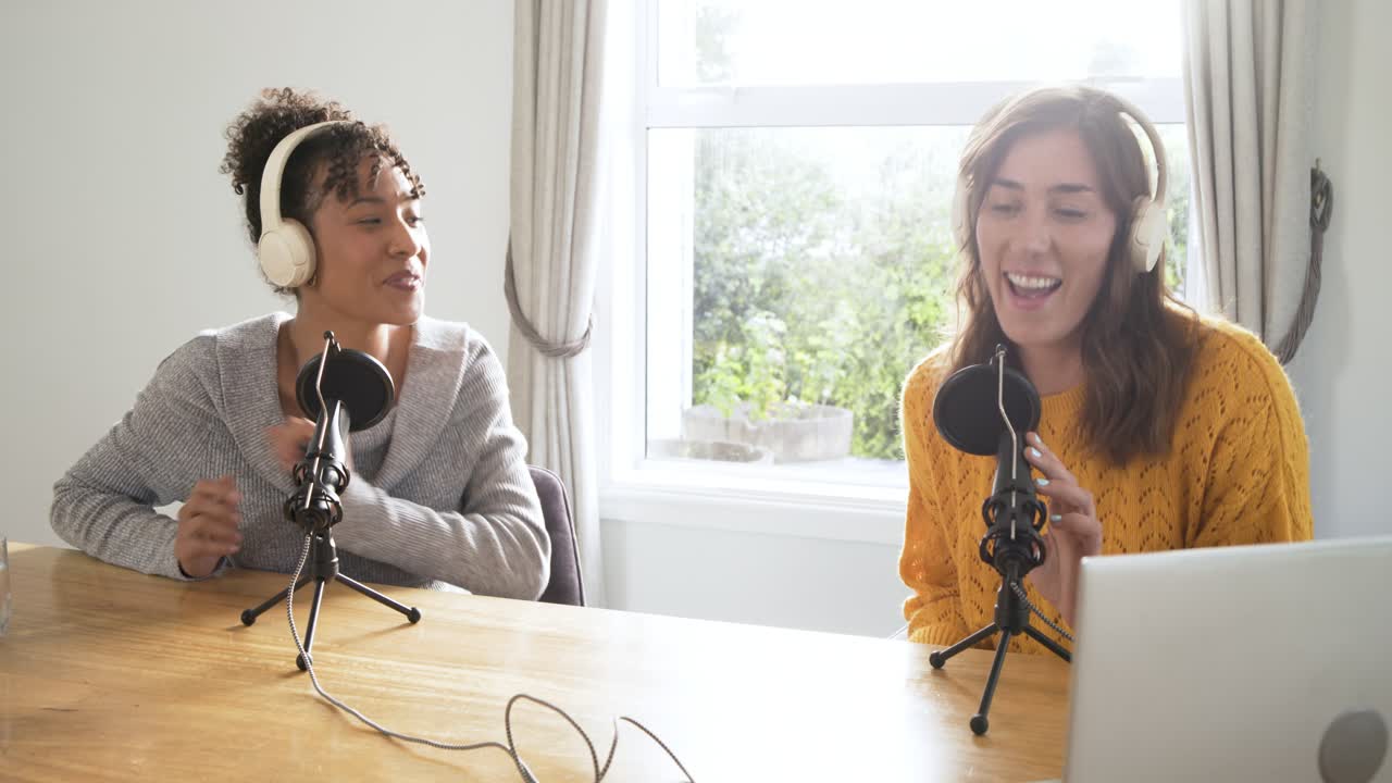 Colegas de trabalho diversas testando microfones, trocando fones de ouvido e começando um bate-papo de podcast na escrivaninha de casa.