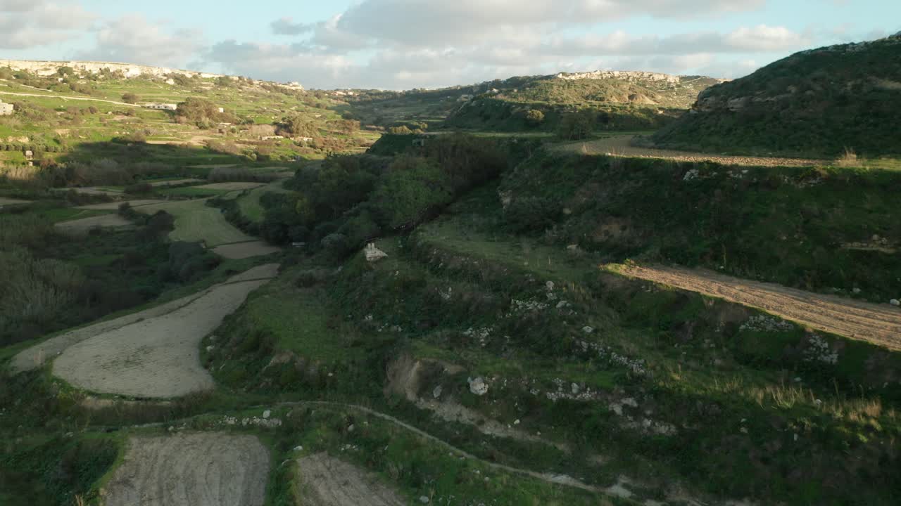 antena: volando sobre tierras de cultivo verdes rocosas en la colina en una tarde soleada en malta