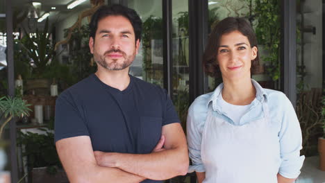 retrato de dueños masculinos y femeninos de floristas de pie en la puerta rodeados de plantas