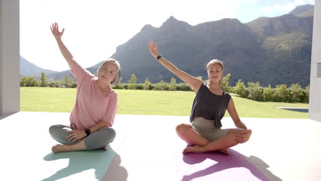 Practicing yoga, two women sitting on mats outdoors in serene mountain setting