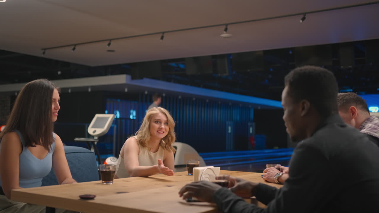 A multi-ethnic group of friends in a bowling club communicate at the table and rejoice in the victory of a friend. Give five