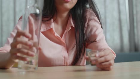 un primer plano de una mujer asiática borracha bebiendo vodka y mirando a la cámara en casa.