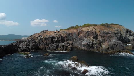 Aerial-pan-shot-around-big-rocks-in-the-sea-next-to-the-shore-in-sunny-summer-day-1