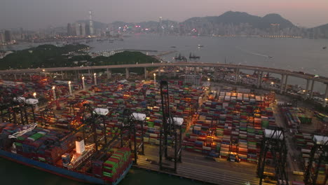 wide angle drone shot after sunset of traffic driving over an elevated highway with a great view on the skyline of hong kong and the container port