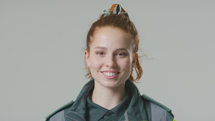Studio Portræt af smilende ung kvindelig paramediciner mod almindelig baggrund