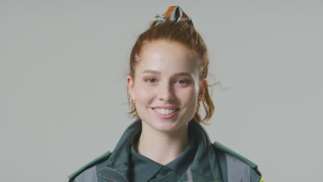 studio portrait of smiling young female paramedic against plain background