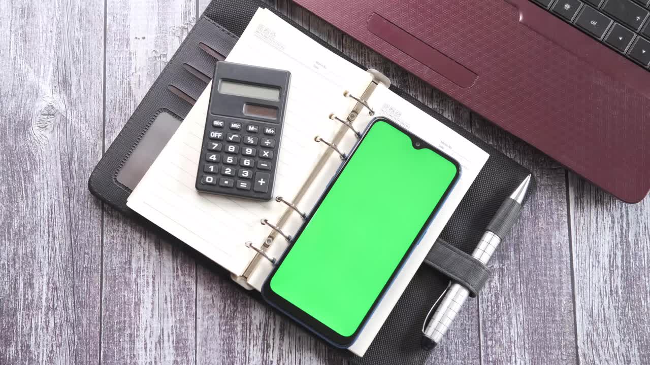Office workspace with notebook, laptop, calculator, phone, and pen