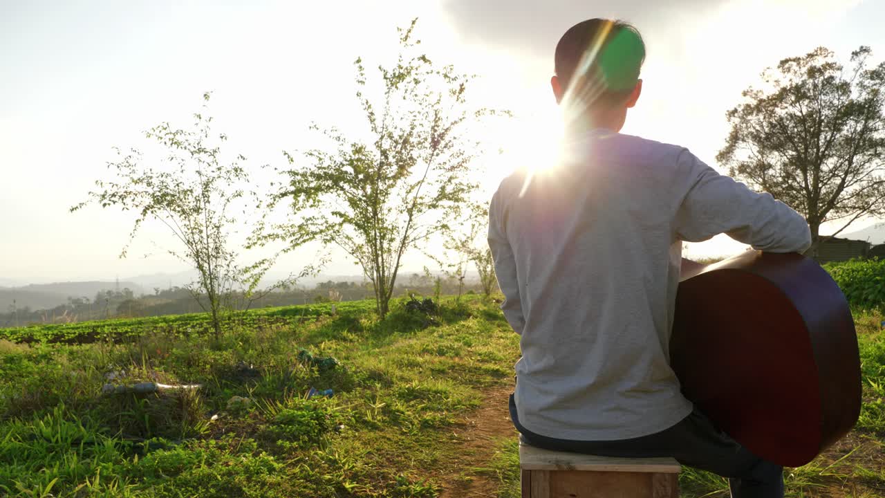 베트남, 태양이 빛나고 조명탄과 함께 앉아 기타를 연주하는 남성 음악가의 뒤에서 보기