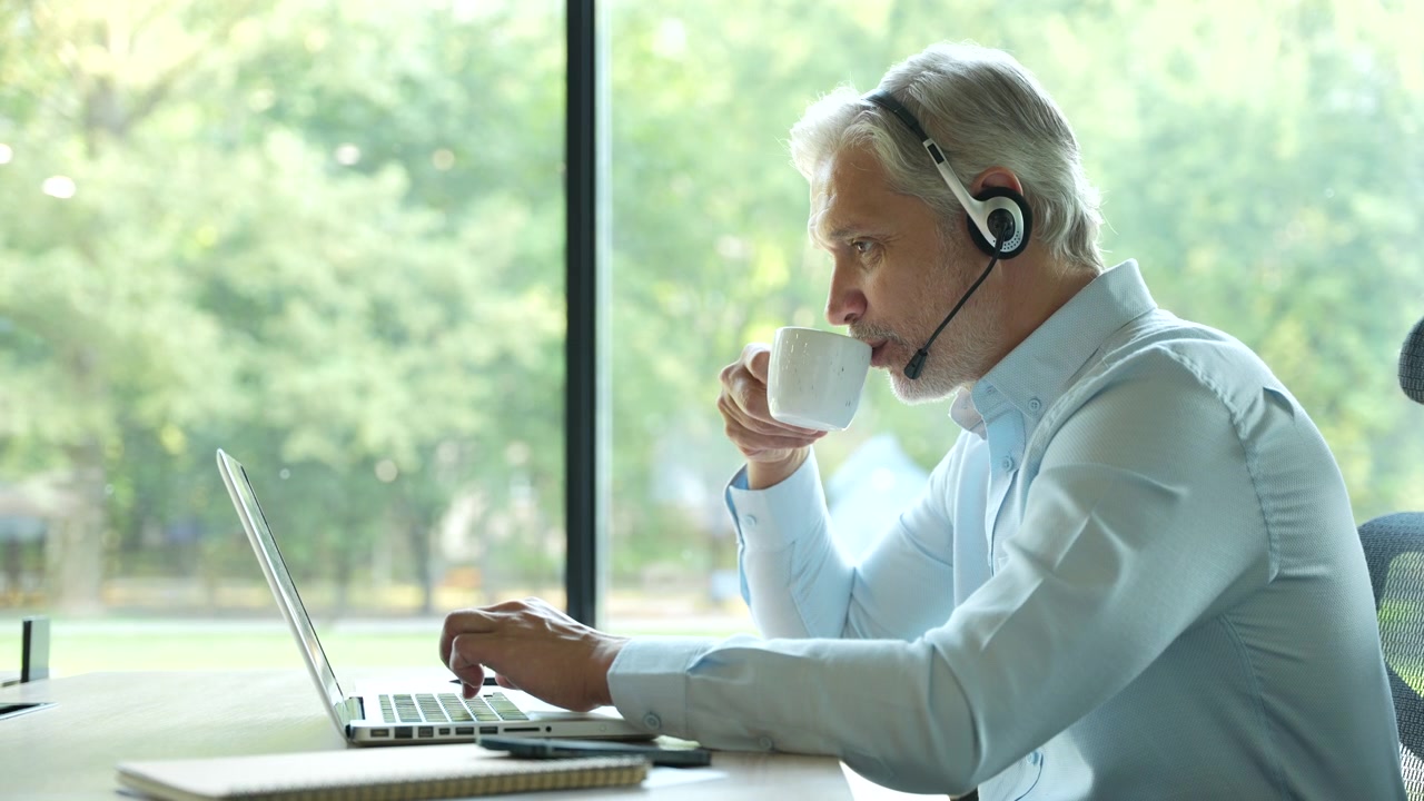 Moden forretningsmand arbejder på bærbar computer med headset på moderne kontor