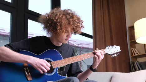 a curly red-haired boy of american appearance is learning to play the guitar. guitarist’s hand close-up. education and hobbies.