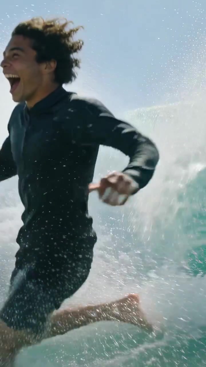 Video vertical: Hombre con traje de neopreno corriendo hacia las olas mientras una ola rompe, con espacio para texto.
