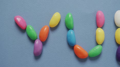 video of overhead view of yummy text formed multi coloured sweets over blue background