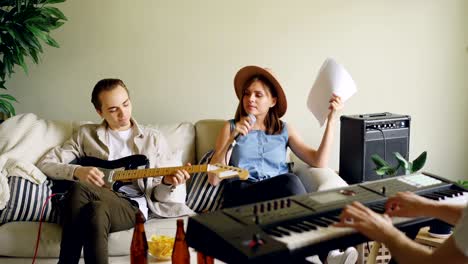 cheerful young people musical group are practising in home studio singing and playing the keyboard and the guitar. musicians are wearing casual clothes.