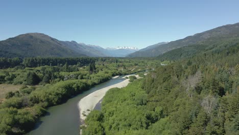 aerial dolly in of rio azul stream between pine tree woods with mountains in background, patagonia argentina