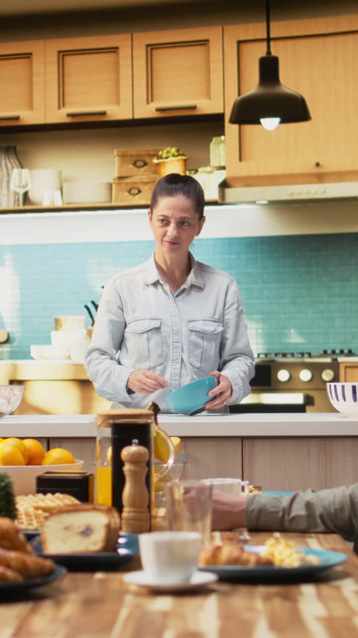Vertical Video Mother preparing breakfast in the morning light while family waits at the table