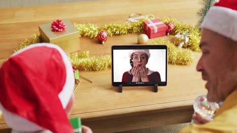 padre y hijo caucásicos con sombreros de santa usando una tableta para una videollamada de navidad con una mujer en la pantalla