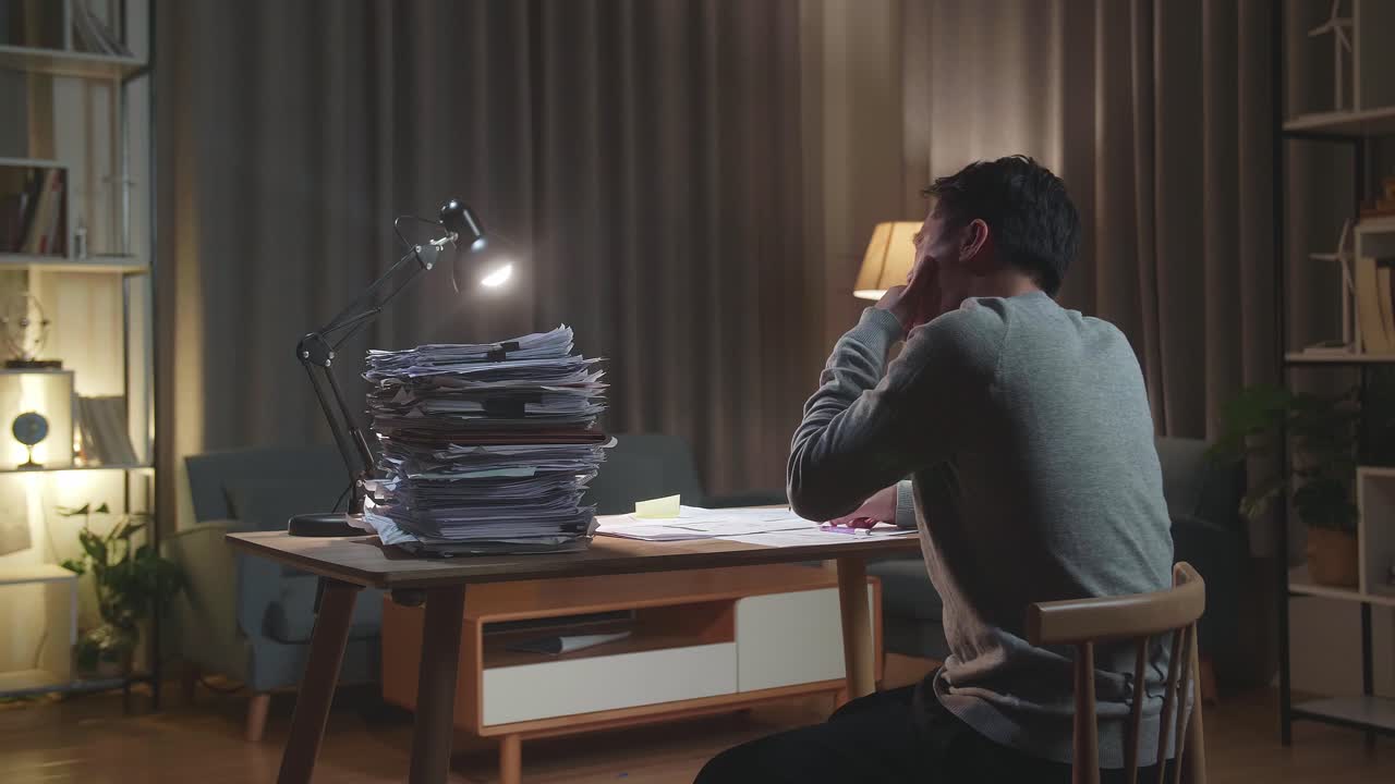 Back View Of Tired Asian Man Yawning And Taking Off His Glasses Before Sleeping While Working Hard With Documents At Home