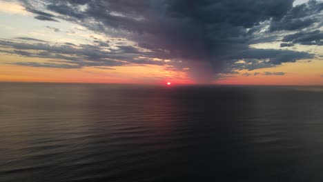 Drone-shot-of-sun-rising-or-setting-with-a-moody-dark-cloud-over-the-ocean-in-50fps