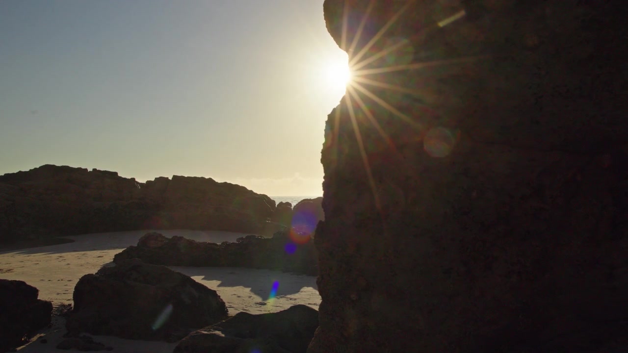 Destello solar junto a roca costera oscura en playa de arena en Portugal