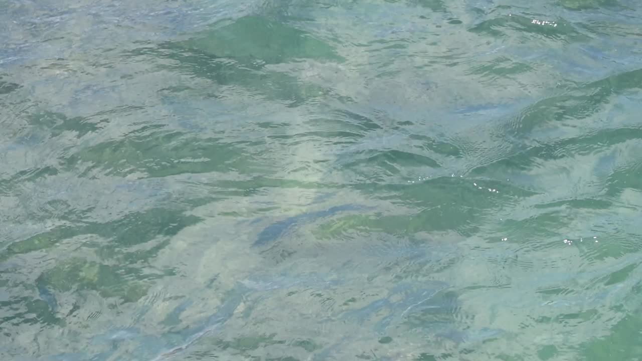 A detailed view of soft ripples on clear, greenish-blue water, capturing the fluid movement and texture.