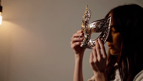 woman holding and adjusting an ornate golden mask
