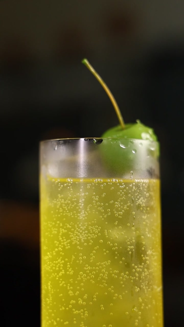 Cocktail giallo gassato rinfrescante con guarnizione di ciliegia verde