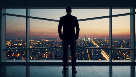 businessman overlooks city skyline from a high-rise office at dusk