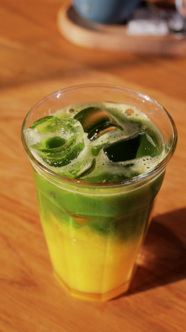 Close up of a glass of an iced orange juice matcha on a table at a cafe. Vertical