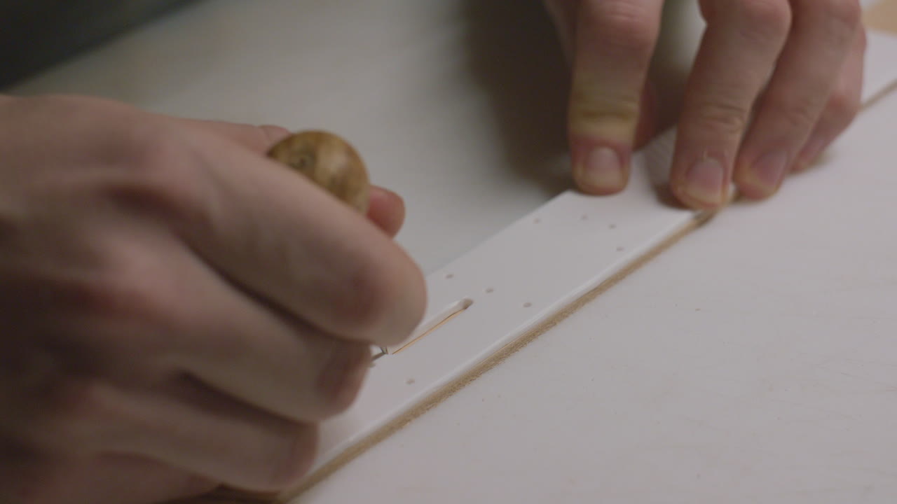 A detailed close-up of a craftsman carefully marking leather with an awl using a template for precision.