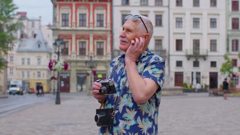 turista anciano con cámara de fotos retro, sonriendo, escuchando música auriculares, bailando en la calle
