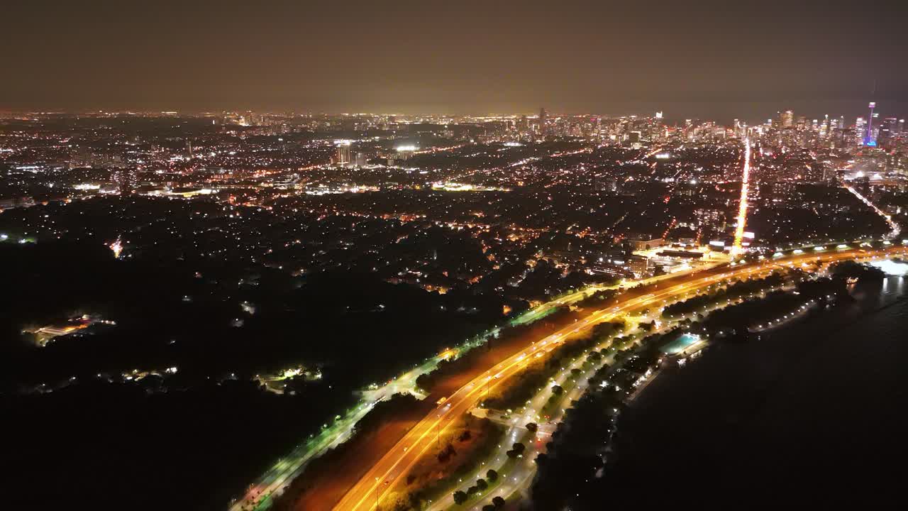 Aerial: Gardiner Expressway at night with cityscape and Lake Ontario in Toronto, Ontario, Canada, establishing drone shot