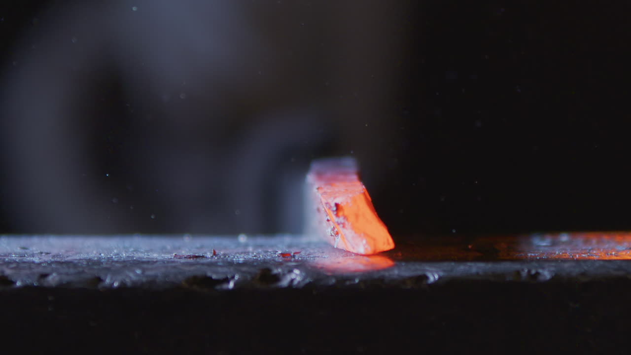 Metalsmith forges hot iron piece on anvil with hammer, slomo closeup slider