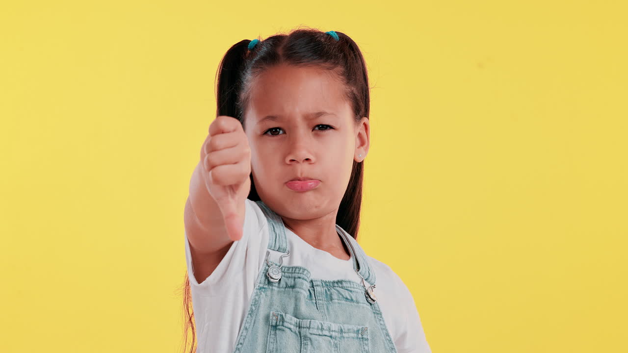 Girl with thumbs down on yellow background