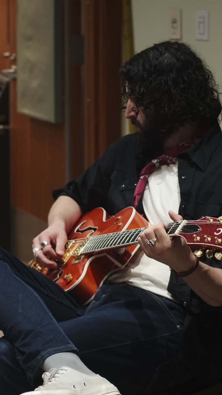 Seated Musician With Curly Hair Strumming On An Electric Guitar In Studio. vertical shot