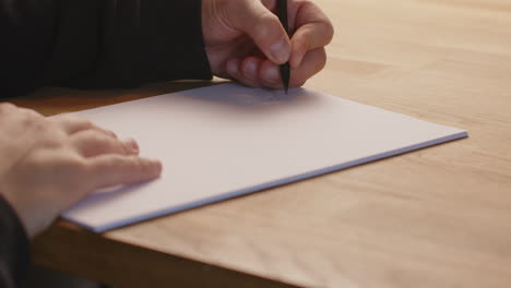 caucasian person writing with the left hand of a peace of paper with a pencil