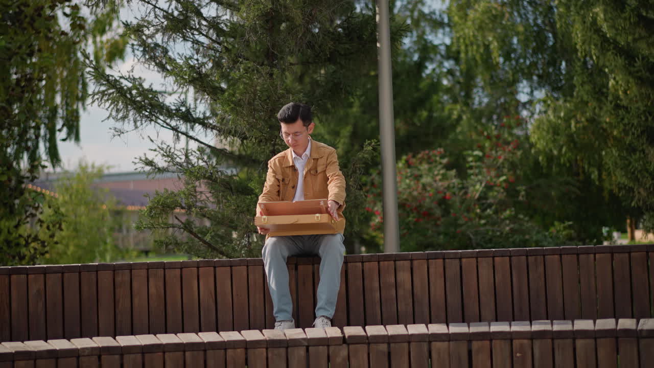 Joven dibujando en un banco de madera en un parque, abriendo una caja de bocetos, estudiando la composición, pintando un boceto a la acuarela, luz de sol otoñal y árboles de fondo, estudiante dibujante y viajero convertido en artista